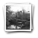 Camponesa com cesto de roupa a atravessar ponte sobre rio