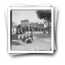 Crianças junto a fontanário com bomba de roda em praça não identificada